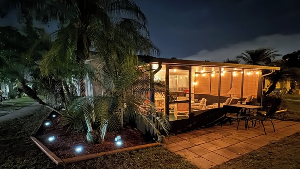 A modern house with a glass exterior, a patio with outdoor furniture, and a well-lit interior. - Fun Open-Concept 2 Bedroom/2 Bathroom Condo w/Screened Porch. 10 Min from Disney (Kissimmee)