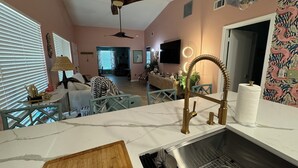 A modern kitchen with a marble countertop, a wooden cutting board, a stainless steel sink, and a ceiling fan. - Fun Open-Concept 2 Bedroom/2 Bathroom Condo w/Screened Porch. 10 Min from Disney (Kissimmee)
