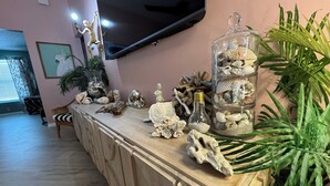 A wooden console table with decorative items, a glass jar with seashells, and a television mounted on the wall. - Fun Open-Concept 2 Bedroom/2 Bathroom Condo w/Screened Porch. 10 Min from Disney (Kissimmee)