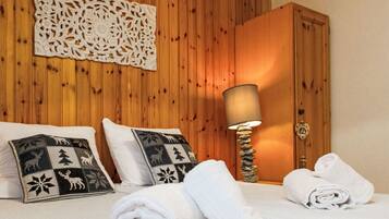 Un lit bien fait, agrémenté de deux coussins décoratifs, une pièce décorative fixée au mur, une armoire en bois et un lampadaire avec un pied en pierre.