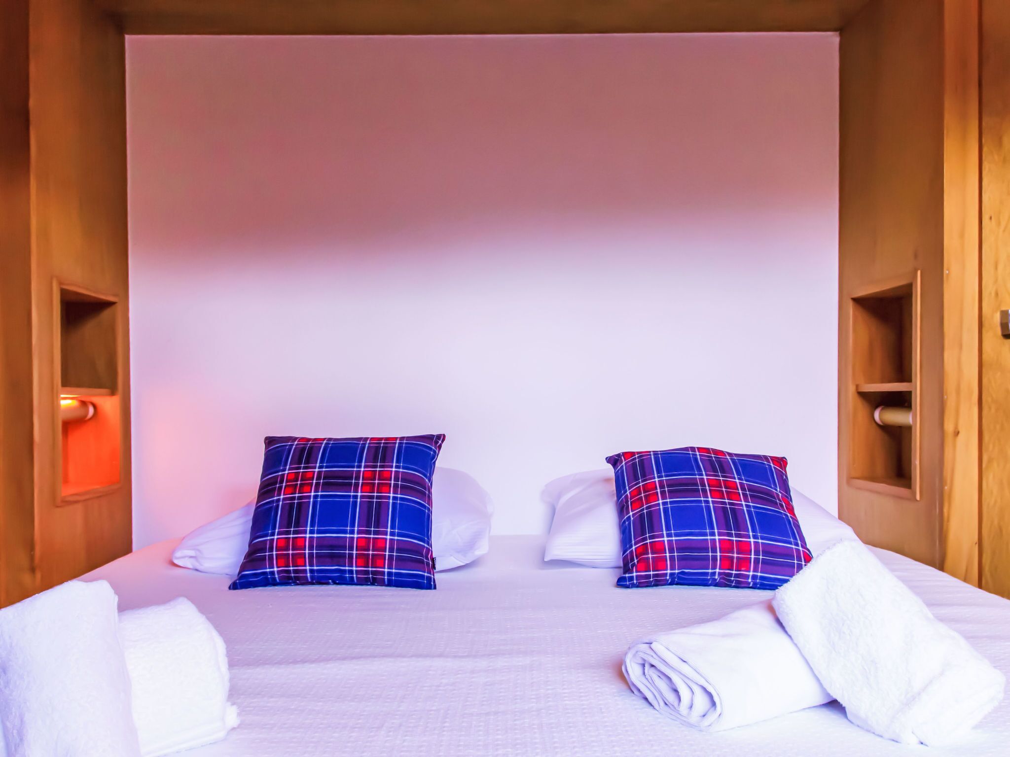 A neatly made bed with two plaid pillows, white pillows, and folded white towels.
