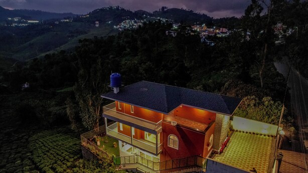 Una casa a due piani con un balcone, immersa nel verde e con dolci colline sullo sfondo.