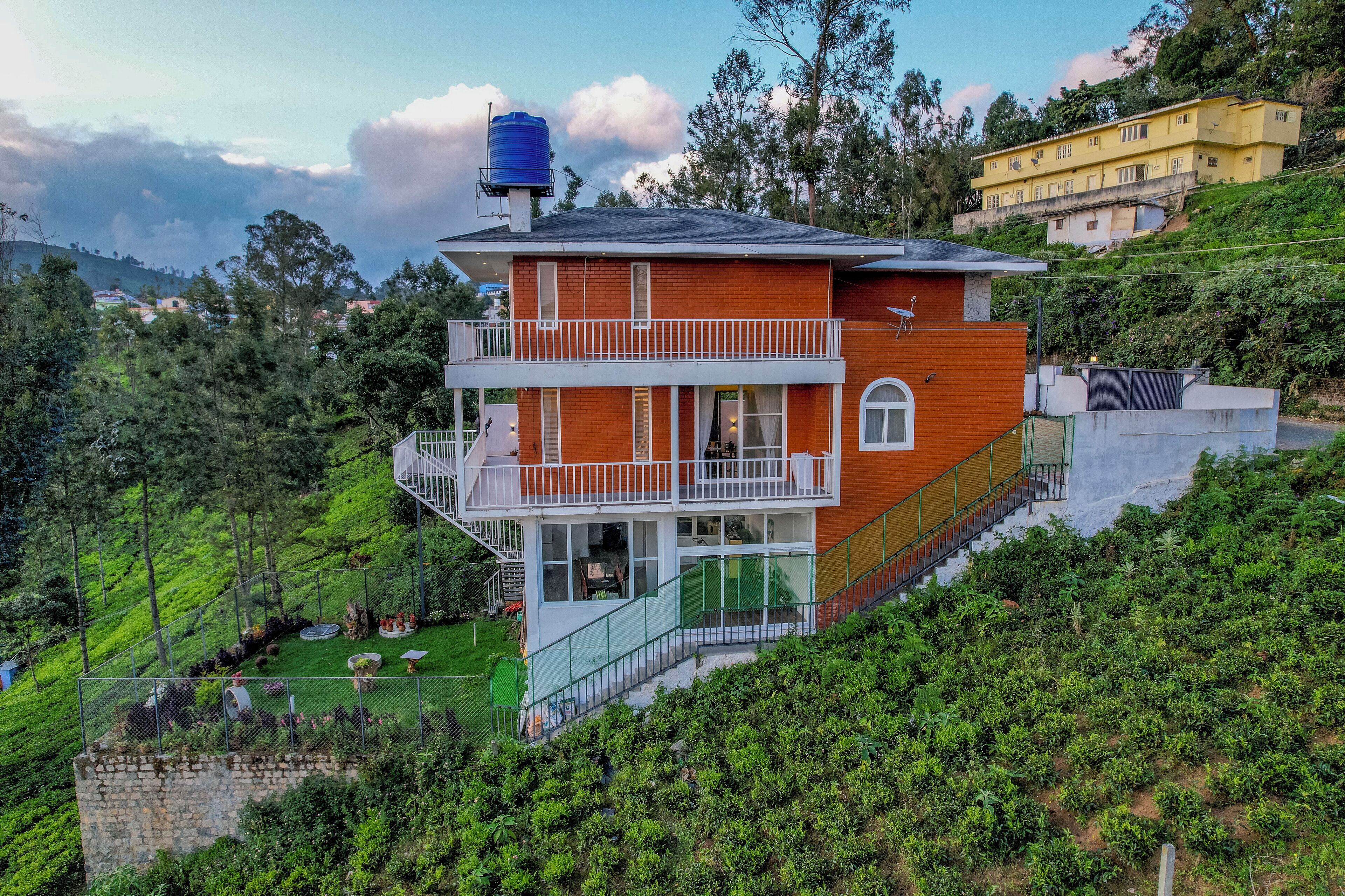 A two-story house with a balcony, surrounded by lush greenery and hills.