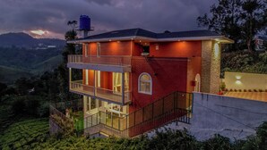Una casa a due piani con un balcone, un serbatoio sul tetto e vista sulle colline circostanti.