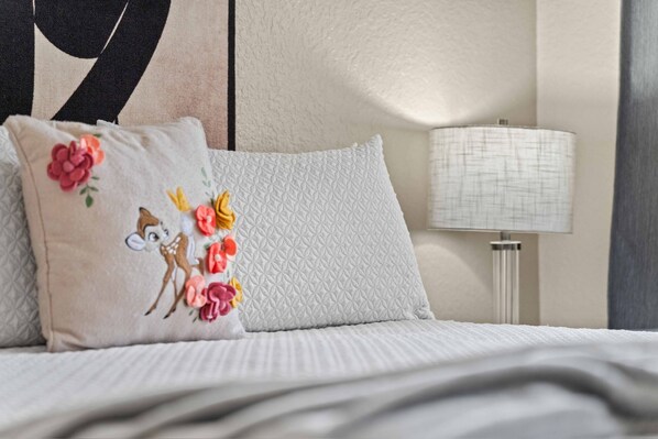 A bed with a quilted pillow and a plain pillow, a bedside lamp, and a partial view of a wall with a geometric design. - Spacious Townhome - 2 King Suites - Pool Access - No Resort Fees - Disney (Davenport)