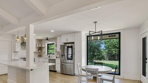 Een moderne keuken met witte kasten, een roestvrijstalen koelkast en een eethoek met een ronde tafel en stoelen.