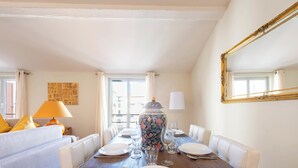 Un coin repas avec une table en bois dressée pour quatre personnes, des chaises blanches, un vase décoré de motifs floraux et un grand miroir accroché au mur.