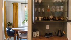 A dining area with a table and chairs, a shelf with glassware and tea sets, and a view of the outdoors.