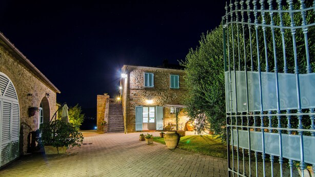 A stone building with a paved entrance, a metal gate, and a well-lit interior. - AgriDepandance Deluxe Cortona Tuscany (Cortona)
