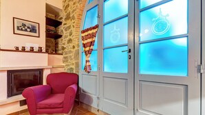 A room with a stone wall, a fireplace, a red armchair, and a door with frosted glass panels. - AgriDepandance Deluxe Cortona Tuscany (Cortona)