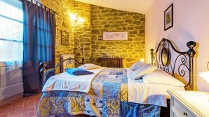 A bedroom with a stone wall, a bed with a patterned bedspread, a nightstand, and a dresser. - AgriDepandance Deluxe Cortona Tuscany (Cortona)