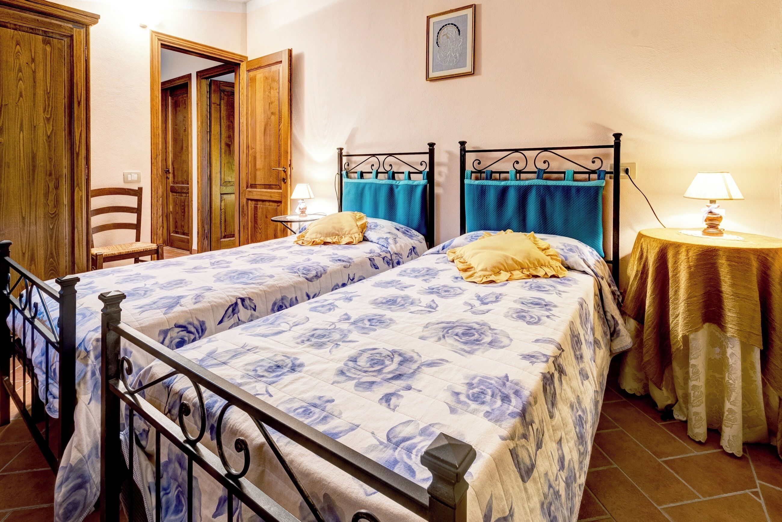 A bedroom with two beds, wooden wardrobe, and a small table with a lamp.