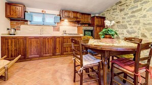 A rustic kitchen with wooden cabinets, a stone wall, and a dining table with chairs. - AgriDepandance Deluxe Cortona Tuscany (Cortona)