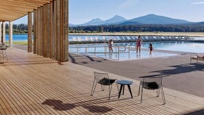 Een buitenzwembad met een houten terras, ligstoelen en uitzicht op bergen en een meer.