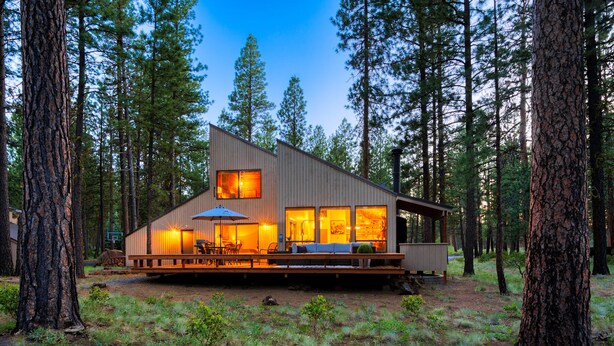 Een moderne chalet met een terras, omringd door hoge dennenbomen.