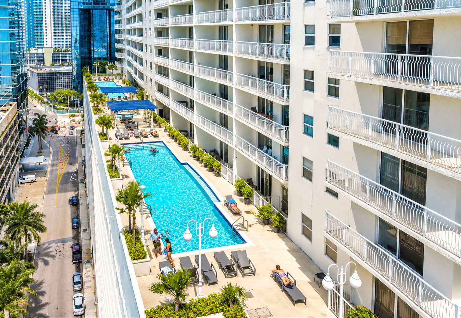 A high-rise hotel with a rooftop swimming pool, multiple balconies, and a view of the surrounding cityscape.