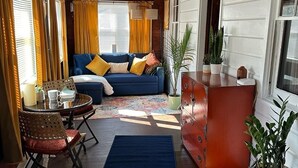 A cozy living room with a blue sofa, wooden furniture, and a large window with curtains. - Charming cottage with lake access, wood burning fire place, and WiFi (Elizaville)