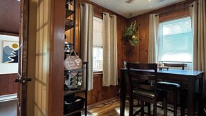 A dining area with a wooden table and chairs, a ceiling fan, and a view of the outside through a window with blinds. - Charming cottage with lake access, wood burning fire place, and WiFi (Elizaville)