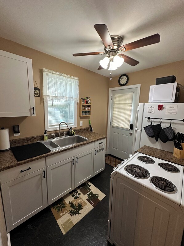 A compact kitchen with white cabinets, a stove, a sink, and a ceiling fan. - Charming cottage with lake access, wood burning fire place, and WiFi (Elizaville)