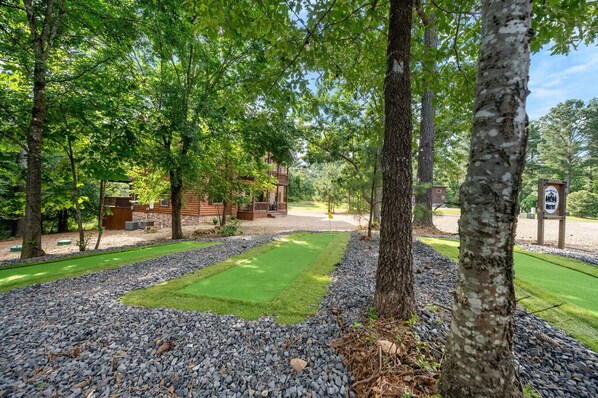 A wooden cabin with a stone foundation, surrounded by a gravel path and lush greenery.