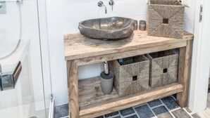 A bathroom with a stone sink, wooden vanity, two wall-mounted lamps, a mirror, and a towel rack.