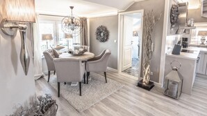 A modern dining area with a chandelier, a round table, and a view of the kitchen.