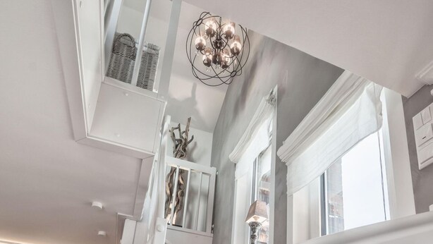 A staircase with white railings and wooden steps, leading to a landing with a chandelier and a decorative wall piece.