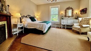 A bedroom with a bed, nightstands, a dresser, a chair, a chandelier, and a fireplace. - Viridia Bed and Breakfast (Littleton)
