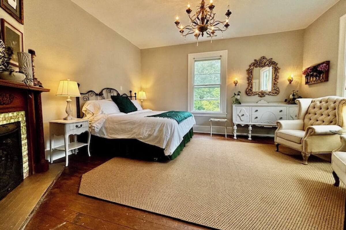 A bedroom with a bed, nightstands, a dresser, a chair, a chandelier, and a fireplace.