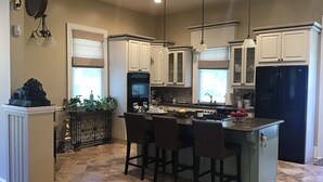 A modern kitchen with white cabinets, a black refrigerator, and a central island with bar stools. - Viridia Bed and Breakfast (Littleton)