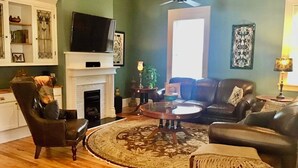 A living room with a fireplace, leather sofas, a coffee table, and a television. - Viridia Bed and Breakfast (Littleton)