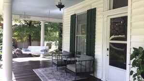 A porch with a swing, a table and two chairs, a chandelier, and a door with a window. - Viridia Bed and Breakfast (Littleton)