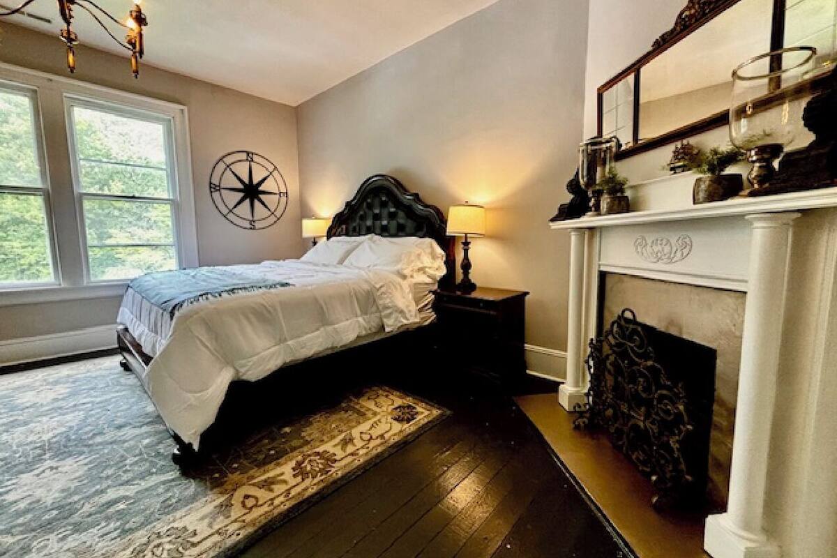 A bedroom with a bed, a fireplace, a nightstand, and a large window.