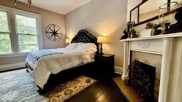 A bedroom with a bed, a fireplace, a nightstand, and a large window.
