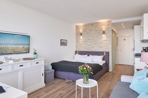 A modern bedroom with a bed, a TV, a desk, and a small table with flowers.