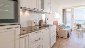 A modern kitchen with white cabinets, a stainless steel range hood, and a large window overlooking the sea.