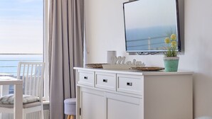 A modern room with a white vanity, a flat-screen TV, a potted plant, and a view of the sea through a large window.