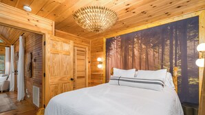 Een houten slaapkamer met een groot bed, een wanddecoratie met bosmotief en een plafondlamp.