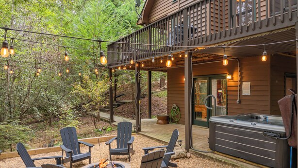Een houten chalet met terras, buitenmeubels, een jacuzzi en lichtslingers.