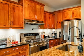 A kitchen with wooden cabinets, stainless steel appliances, granite countertops, and a stainless steel sink.