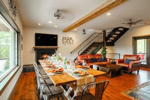 A dining area with a long wooden table set for a meal, a fireplace, and a staircase leading to an upper level. - Winery walk, pickleball and hot tub near Helen (Cleveland)