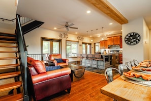 A spacious living area with a leather sofa, dining table set for four, and a kitchen in the background. - Winery walk, pickleball and hot tub near Helen (Cleveland)