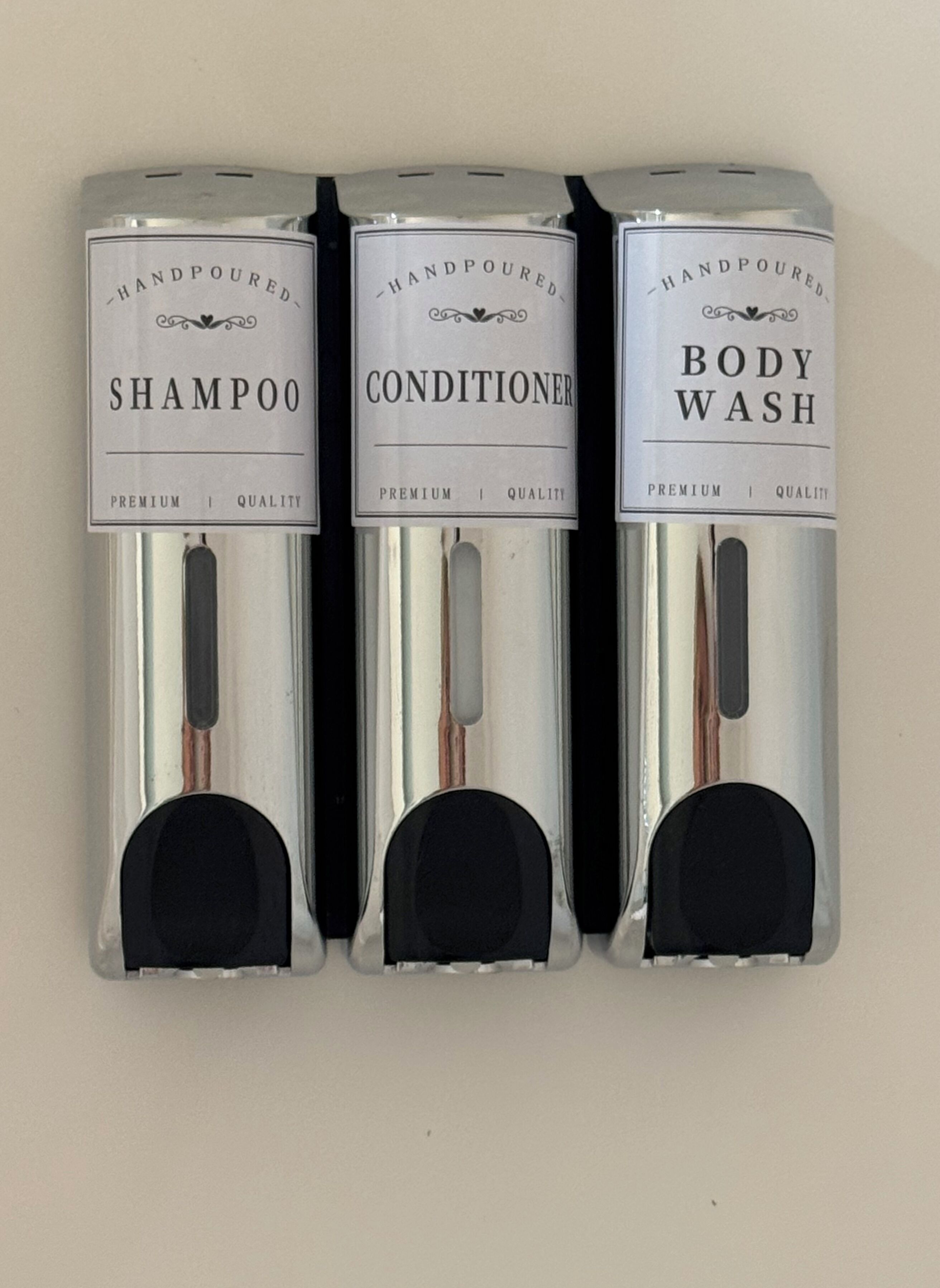 Three handpoured products: shampoo, conditioner, and body wash, each in a silver and black packaging with a label indicating premium quality.