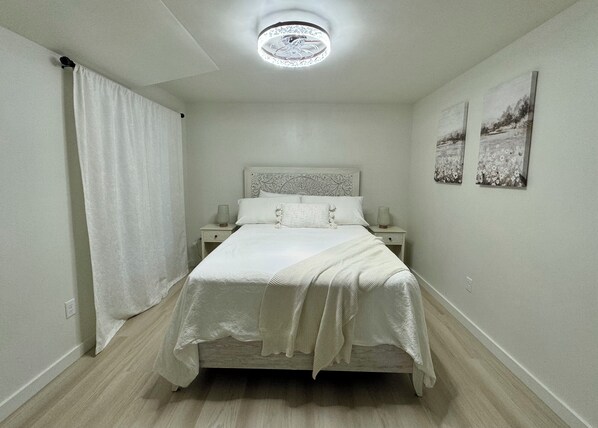 A bedroom with a bed, nightstands, a ceiling light, and two wall-mounted pictures.