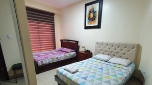 Un dormitorio con dos camas, una mesita de noche, una lámpara y un cuadro en la pared, además de una ventana con persianas.