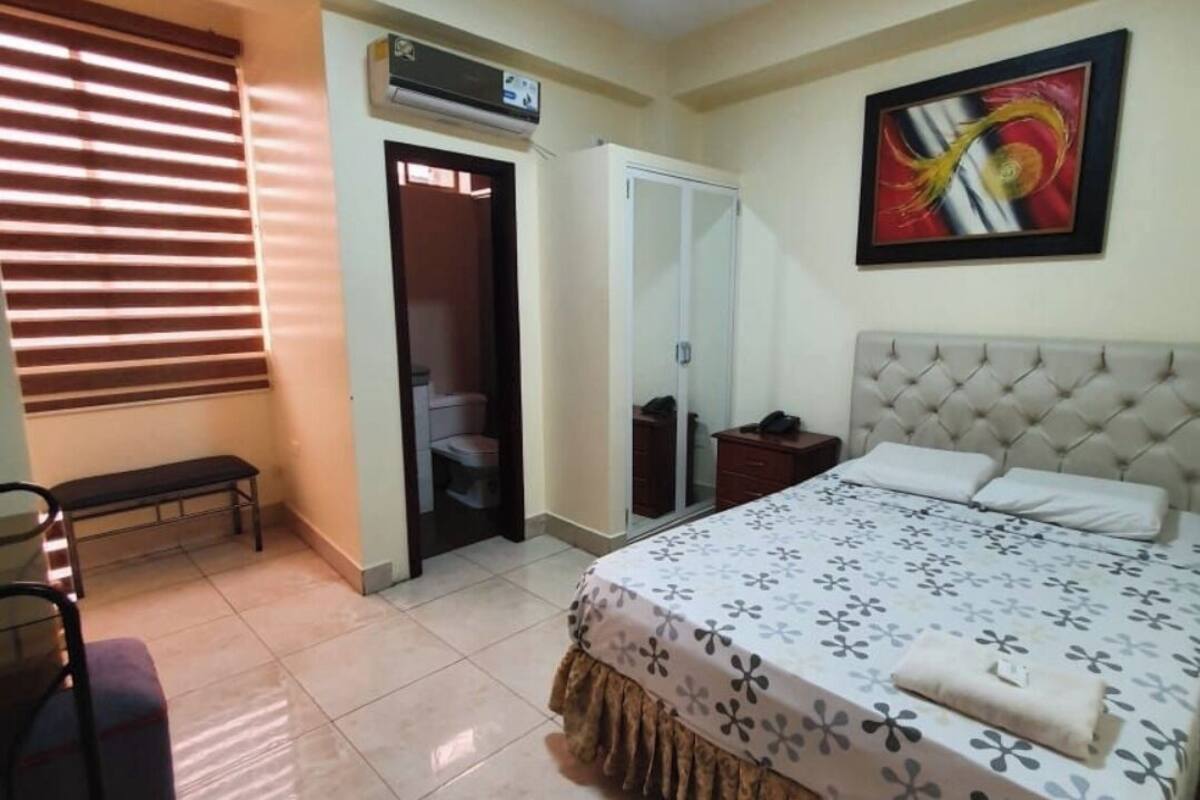 Un dormitorio con cama, un banco, un armario y una puerta que da a un baño.