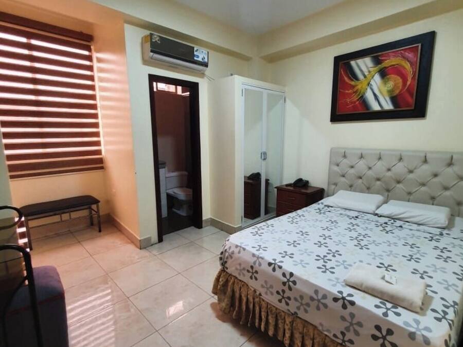 Een slaapkamer met een bed, een bankje, een garderobe en een deur naar een badkamer.