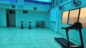 Un gimnasio con cintas de correr, bicicletas estáticas y un estante con mancuernas.