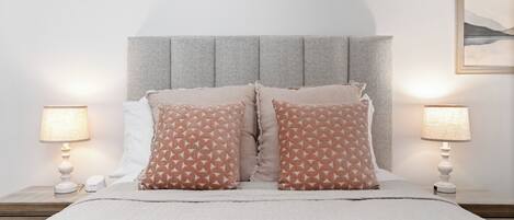 A neatly made bed with a grey headboard, two bedside lamps, and a framed picture on the wall.