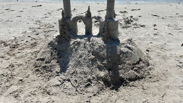 A sandy beach with a sandcastle structure featuring three towers.